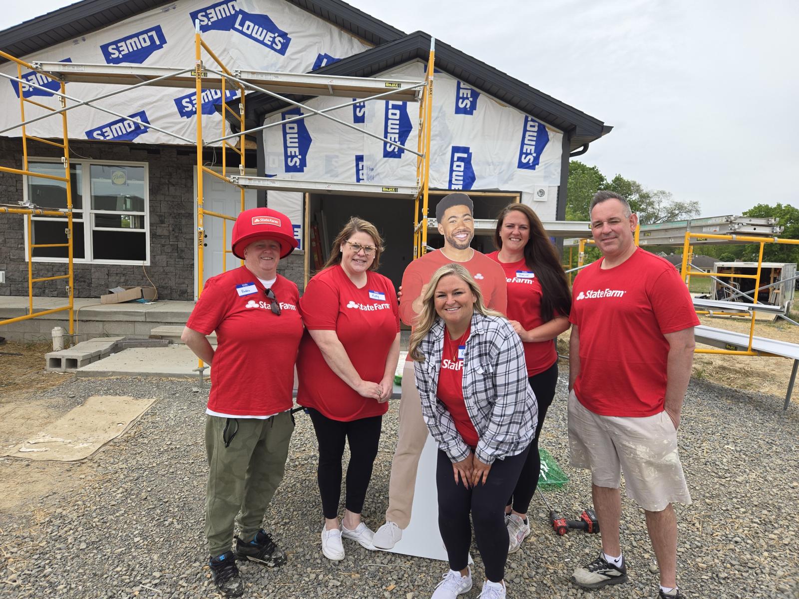 Group of 5 State Farm employees posing in front of a Jake from State Farm cut out and a house under construction.