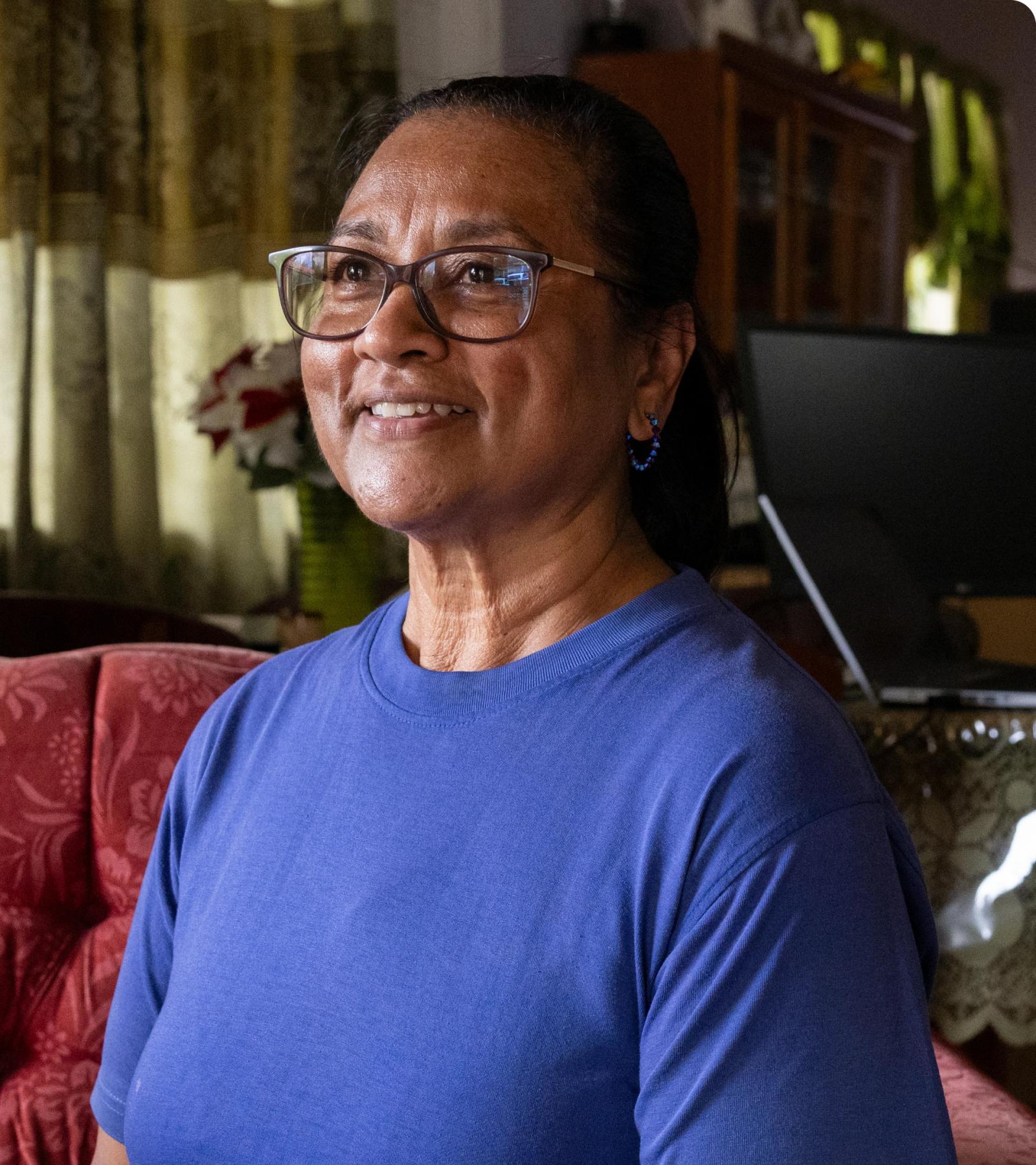 A woman in a blue shirt and glasses smiles at the camera. 