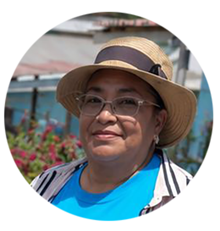 Alba stands in a straw hat and a blue Habitat shirt smiling for the camera.