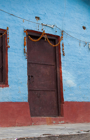 Puerta marrón rodeada de paredes de ladrillo azul con adornos colgando sobre el marco de la puerta.