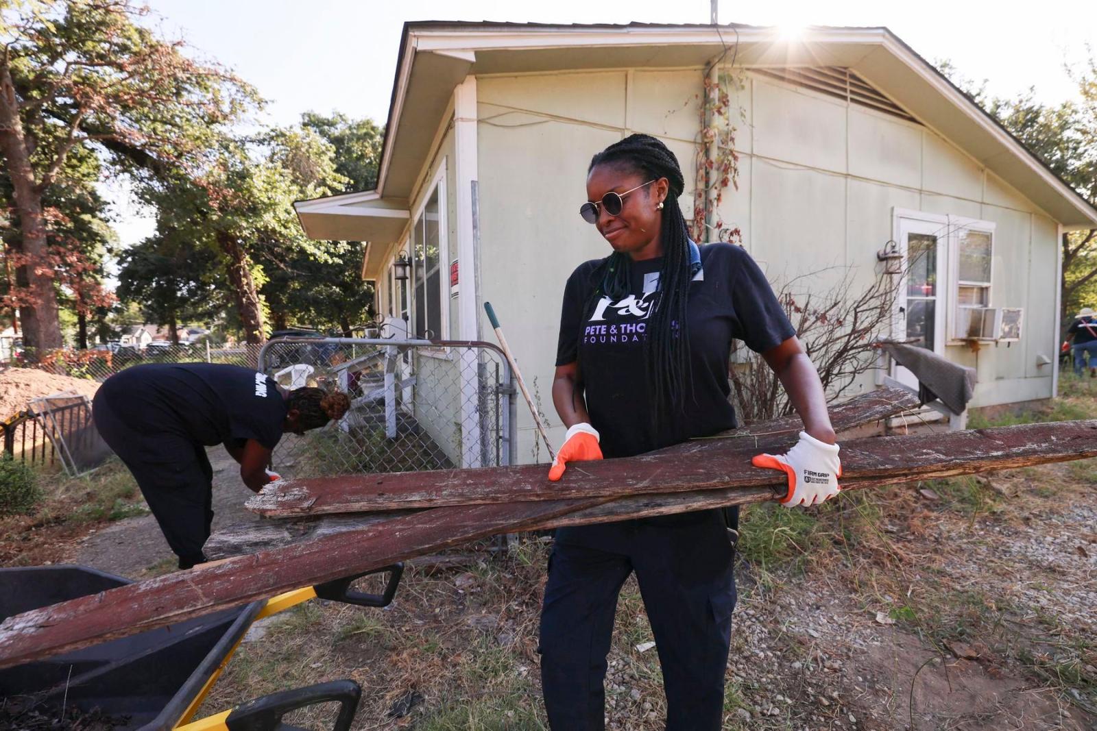 A volunteer in a black Pete & Thomas foundation t-shirt carries a piece of lumber.