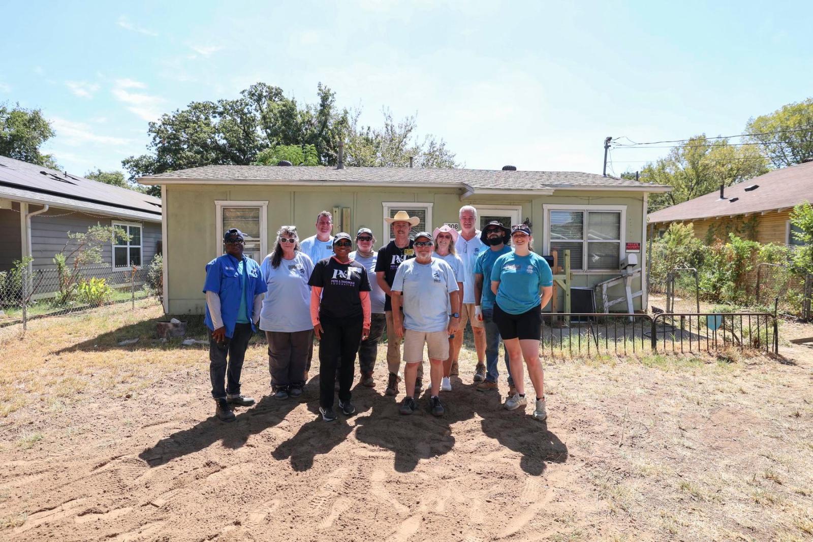 A group of volunteers in Habitat and Pete & Thomas shirts stands in a semi-circle in front of a house they worked on to make aging in place possile.