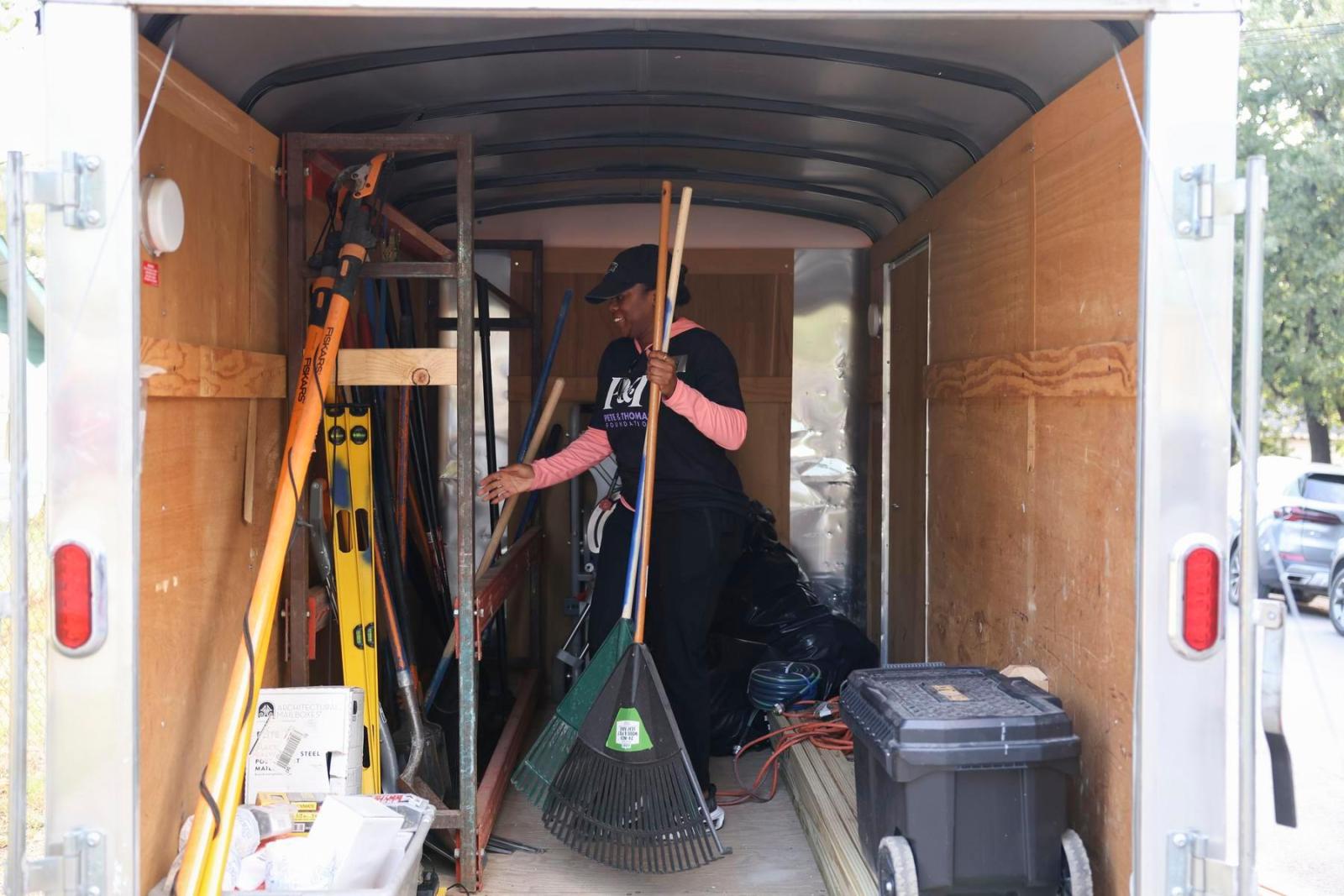 A volunteer stands in the back of a truck holding a rake while gathering other tools.