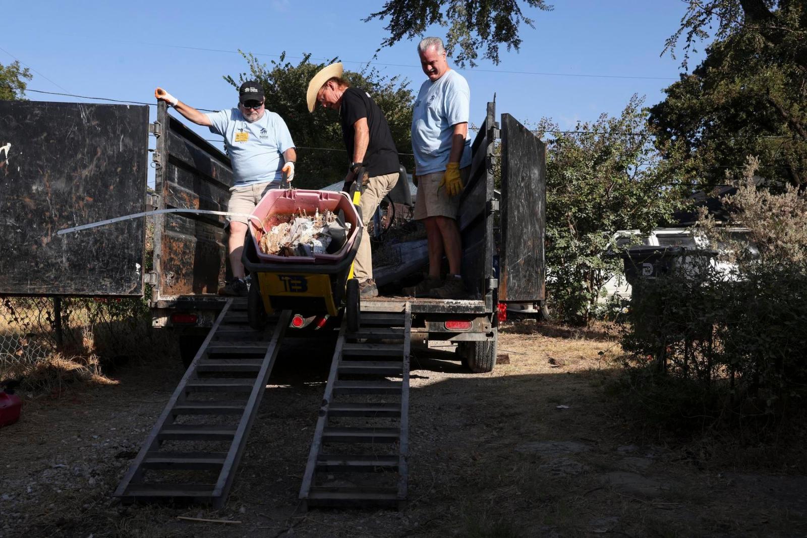 Volunteers stand on the back of a truck and prepare to get equipment down a ramp to street-level.