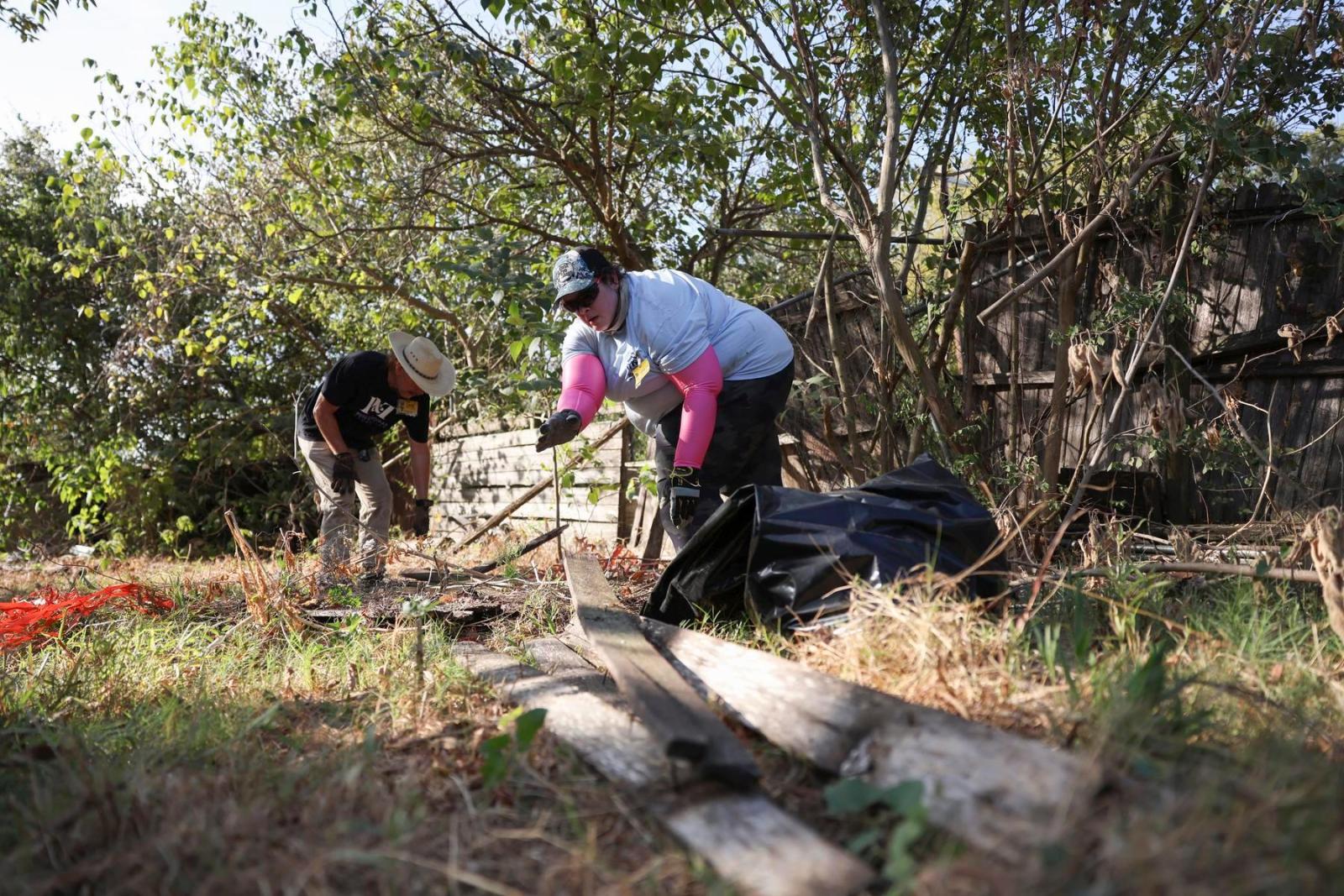 One volunteer in a Habitat shirt and another volunteer in a Pete & Thomas shirt clean up debris in a backyard.