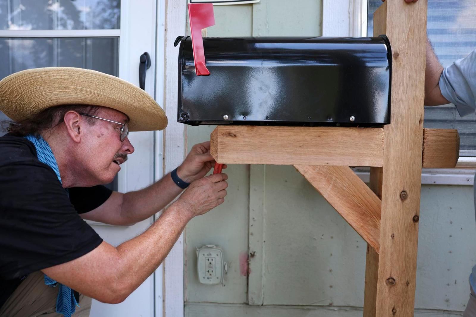 A volunteer bends down to eye-level with a black mailbox on a wooden frame.