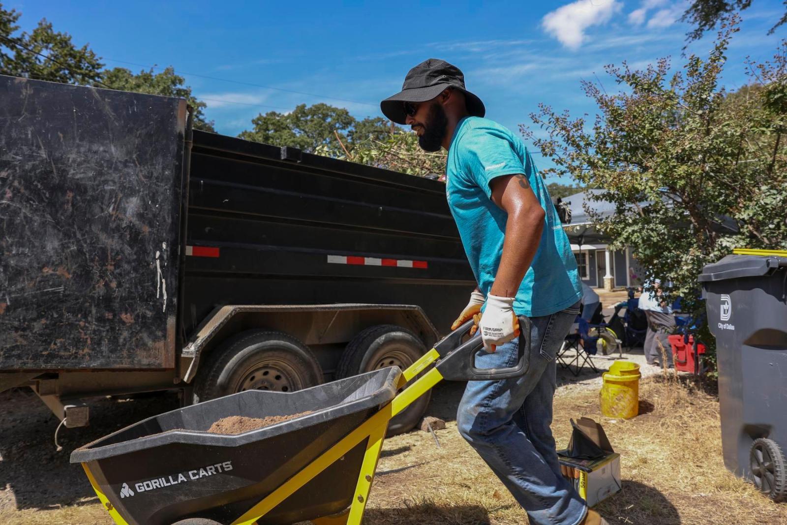 A volunteer wearing a hat pushes a wheelbarrow.