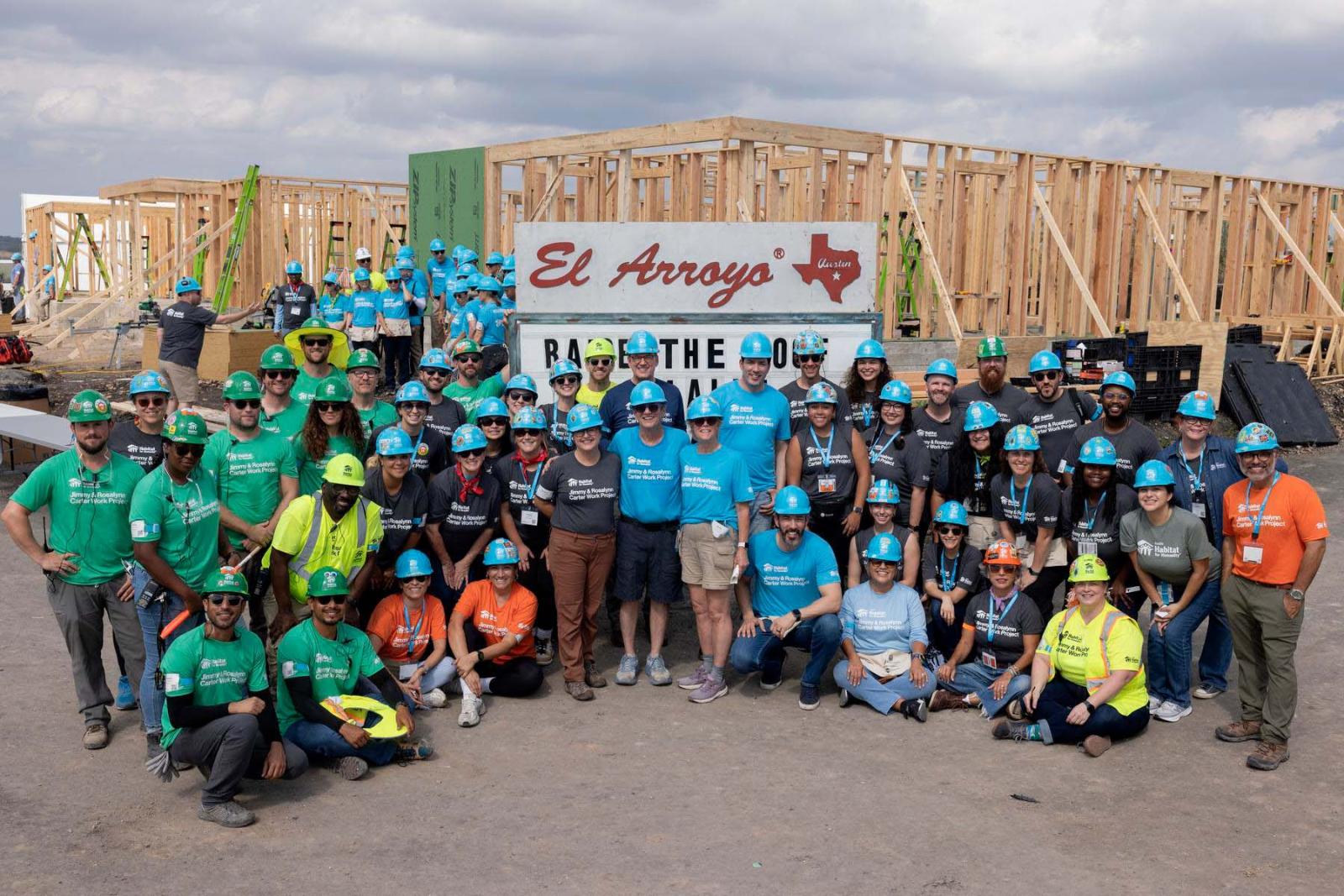 Habitat Austin region volunteers stand in a large group in front of the frame of a house at Carter Work Project in Austin, Texas.