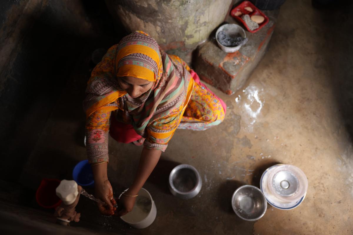 Bangladeshi woman sitting on the ground washing pots in a yellow sari.