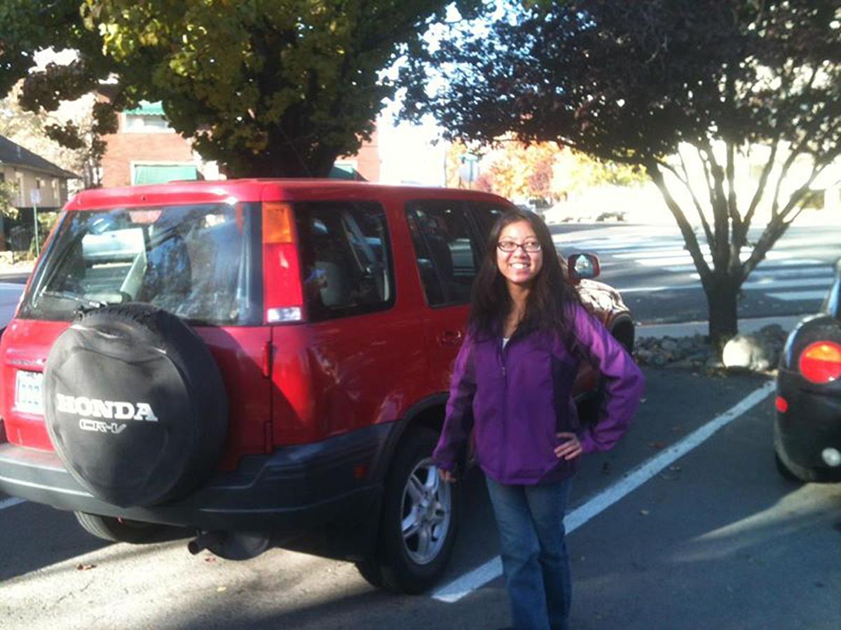 Woman in purple jacket standing next to red SUV.
