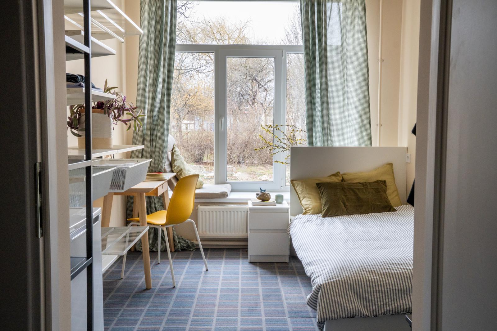 Renovated Ukraine apartment with a tile floor, desk, shelving and bed in a sunlit room.