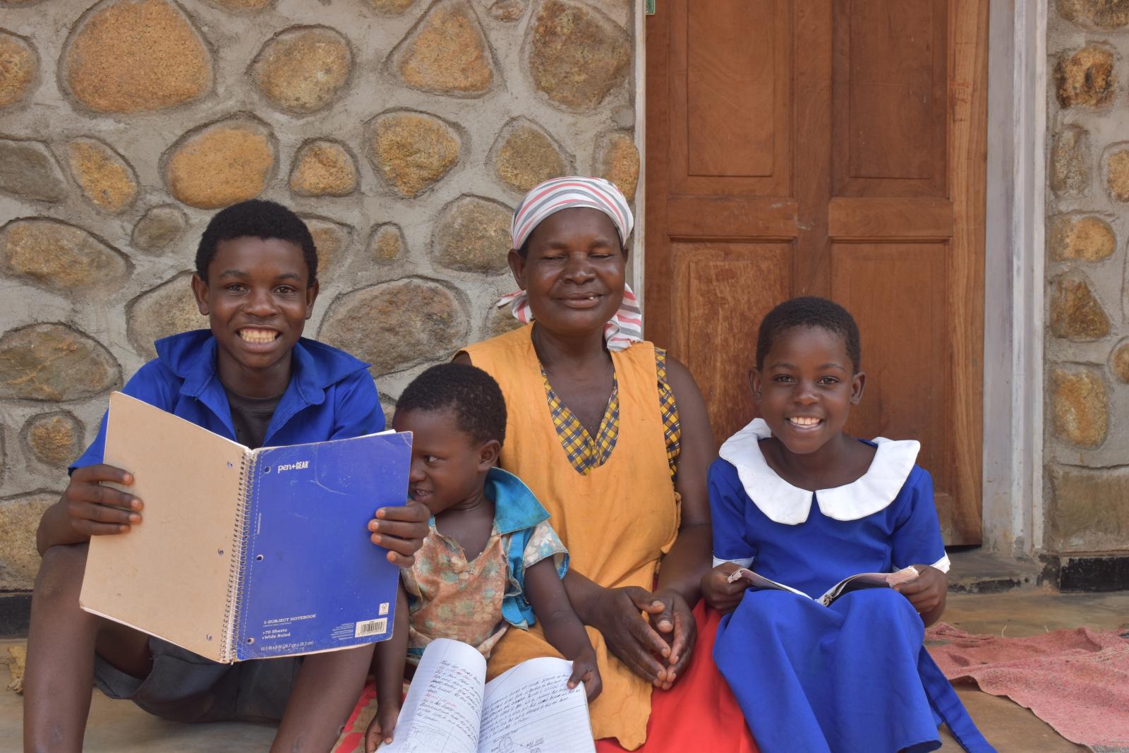 A woman and three children sit outside their home smiling