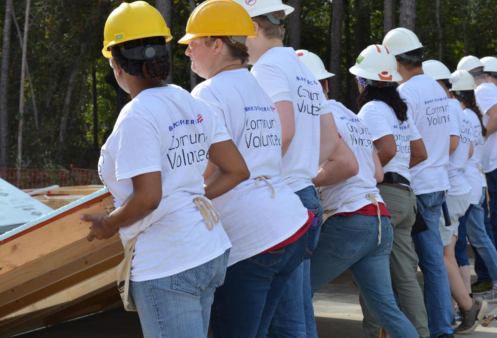 Bank of America employees with hard hats on raising a wall. 