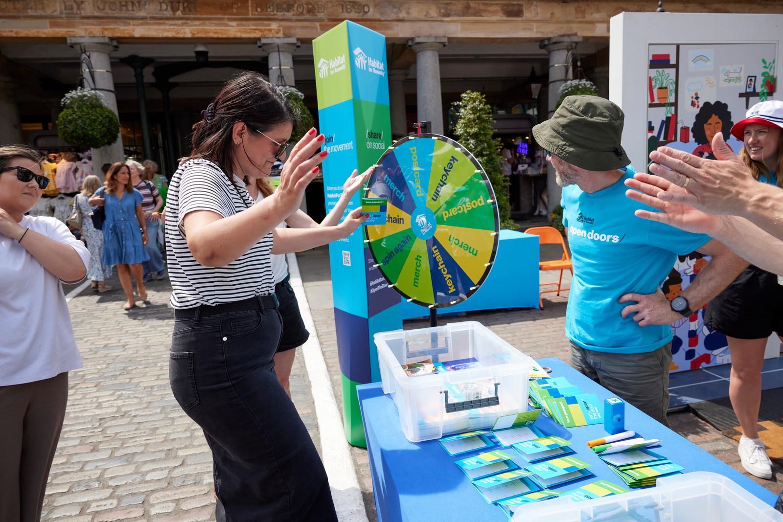 Woman in black pants and a striped shirt participating in a game and spinning the wheel at the Habitat exhibit booth.