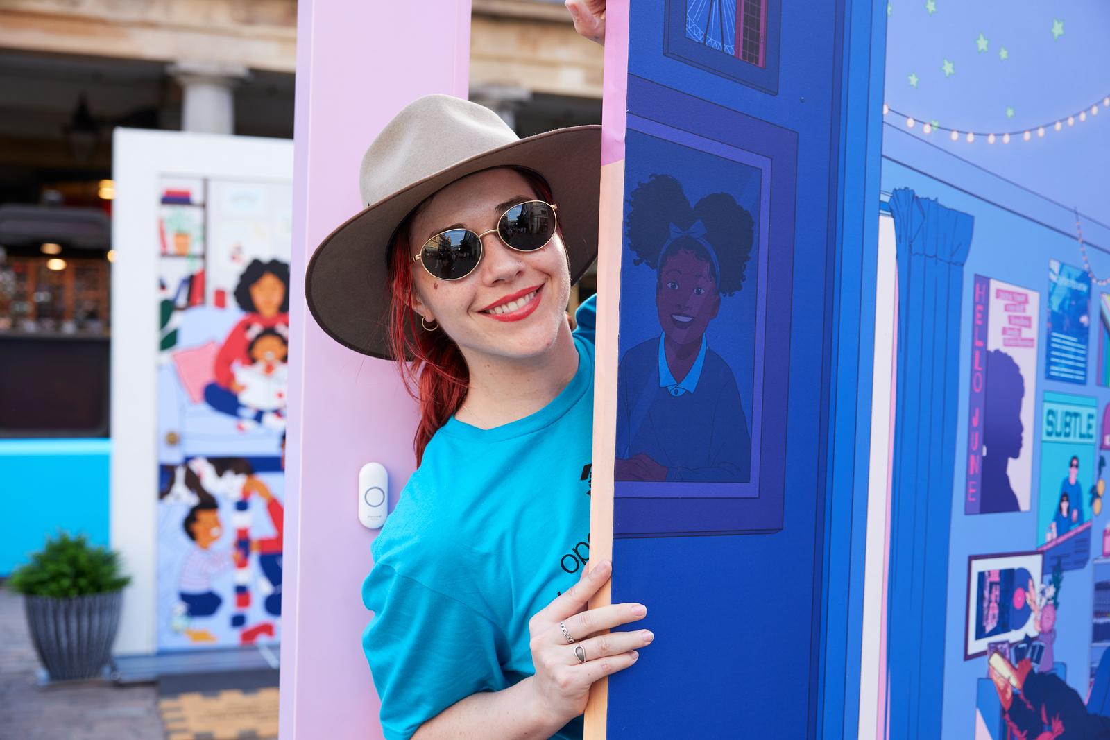 A woman with a tan hat and blue shirt posing with an illustrated door.