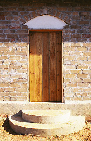 Brown wooden door with a white arch above it and a semi-circle concrete stoop in front.