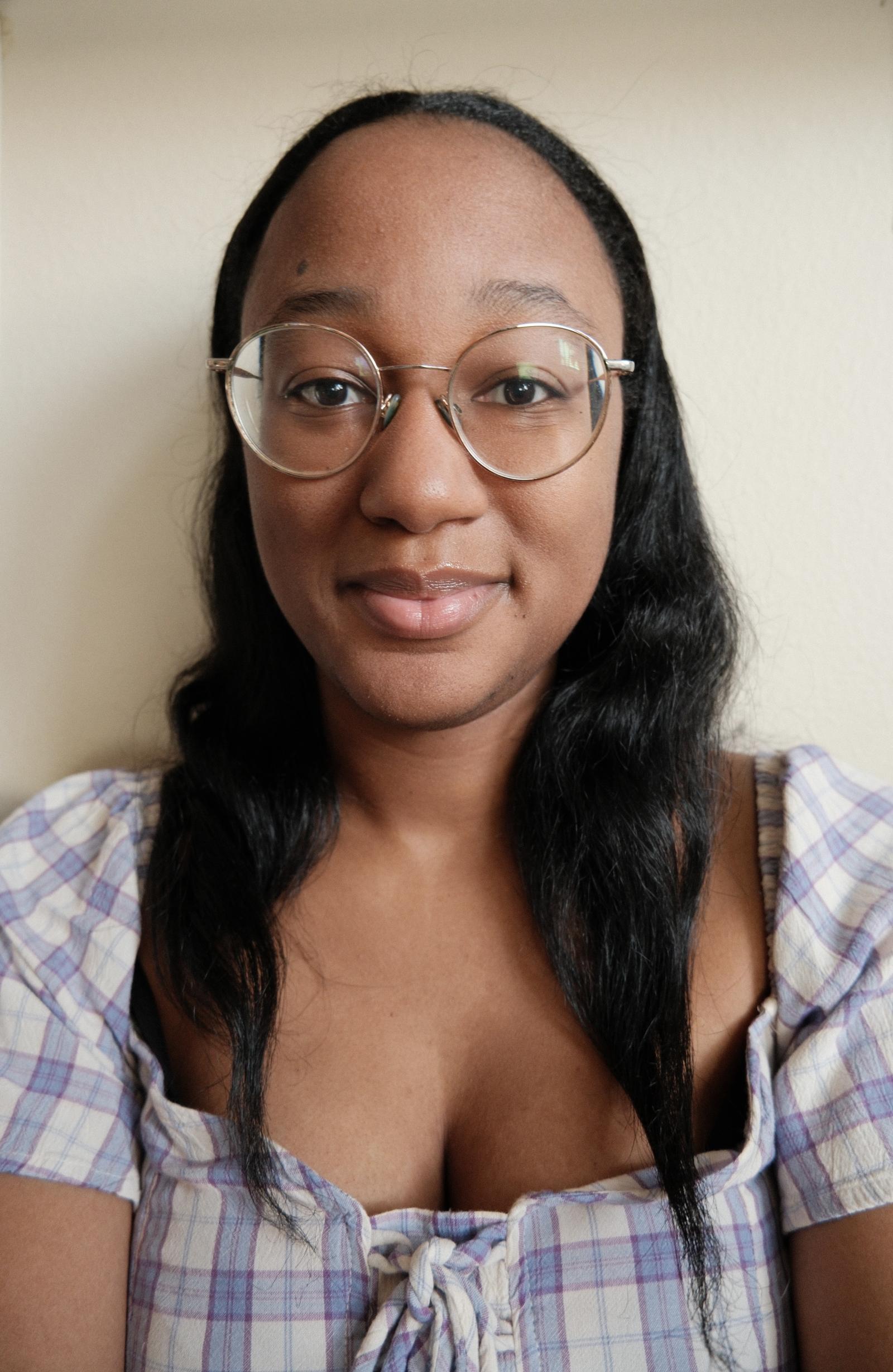 Headshot of woman in a blue and white checkered dress, medium length black hair, and round rimmed glasses.