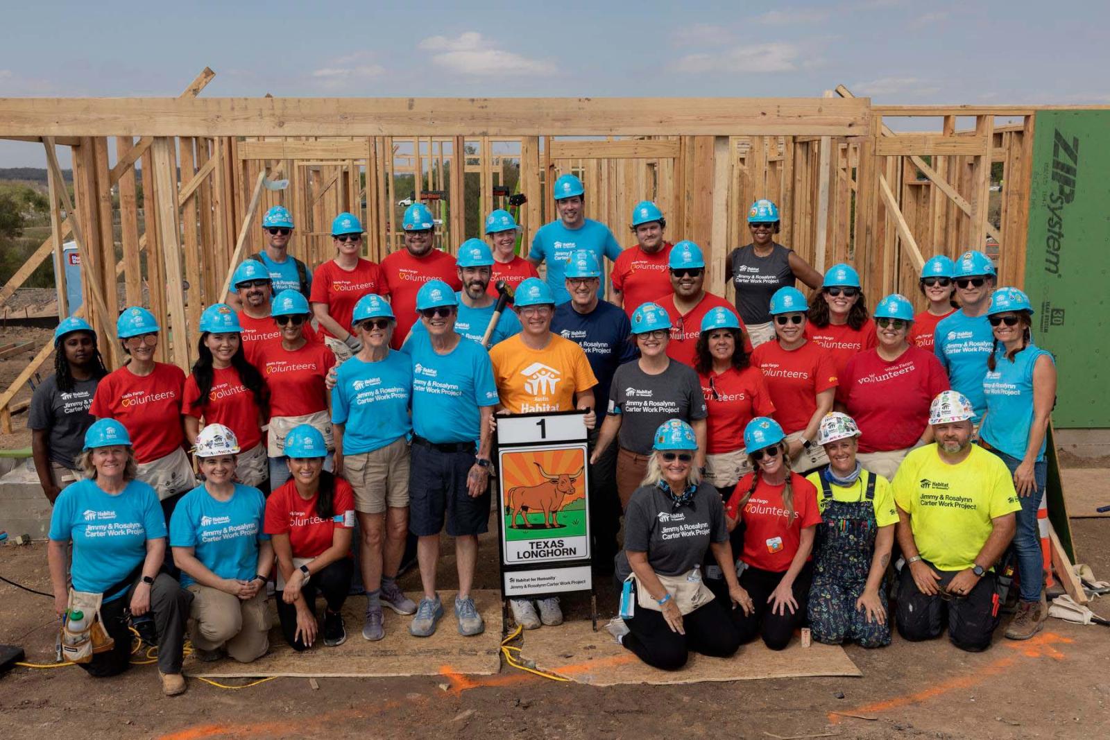 House one volunteers stand in a large group in front of the frame of a house at Carter Work Project in Austin, Texas.