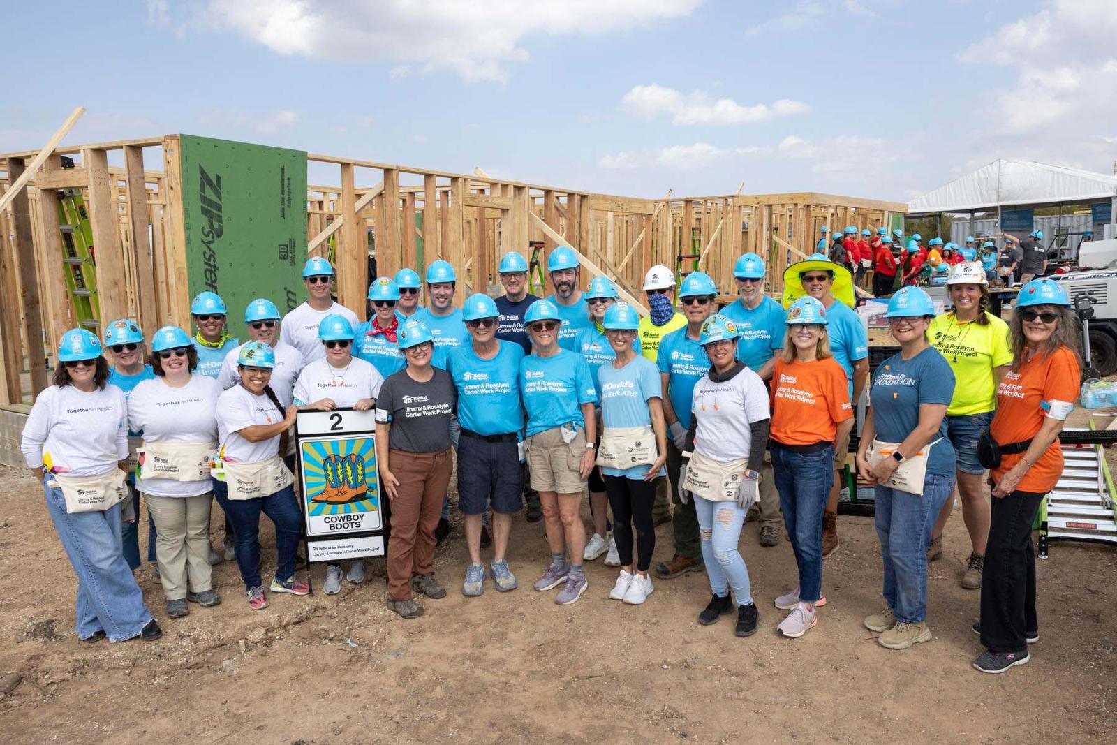 House two volunteers stand in a large group in front of the frame of a house at Carter Work Project in Austin, Texas.