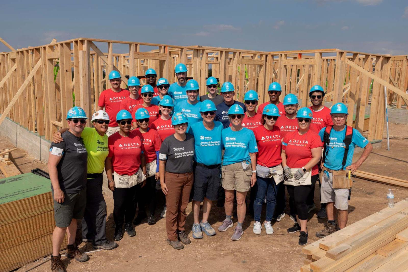 House three volunteers stand in a large group in front of the frame of a house at Carter Work Project in Austin, Texas.