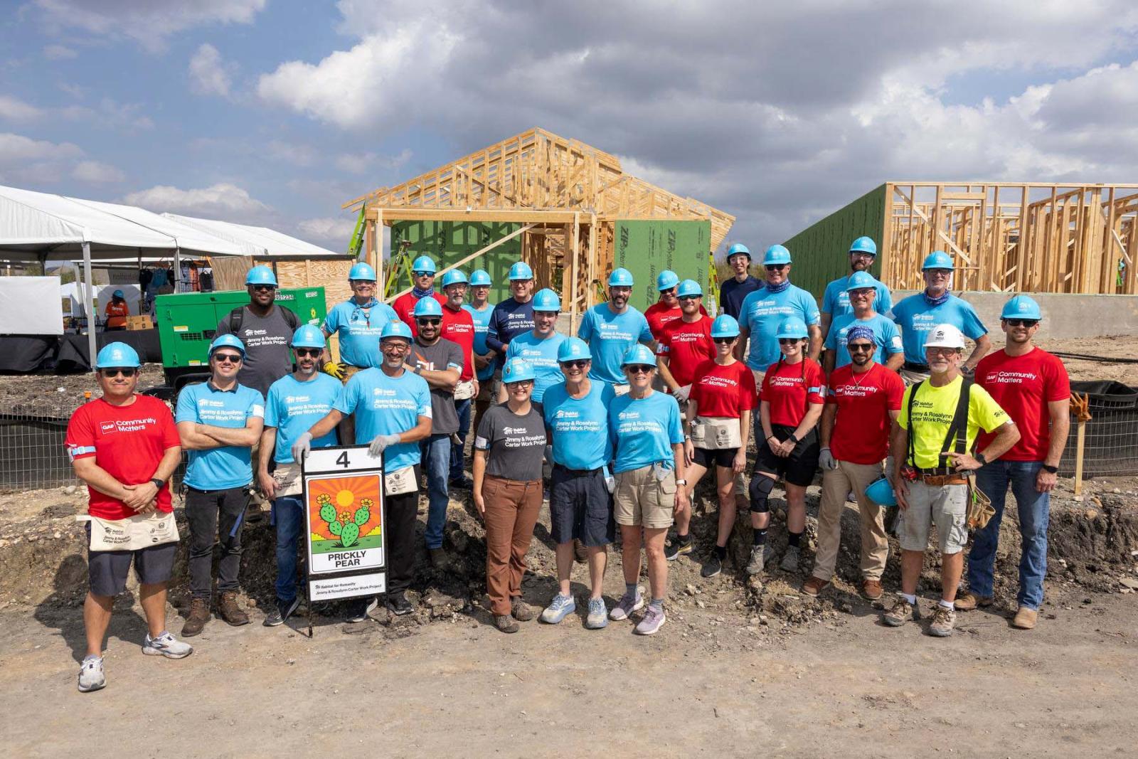 House four volunteers stand in a large group in front of the frame of a house at Carter Work Project in Austin, Texas.