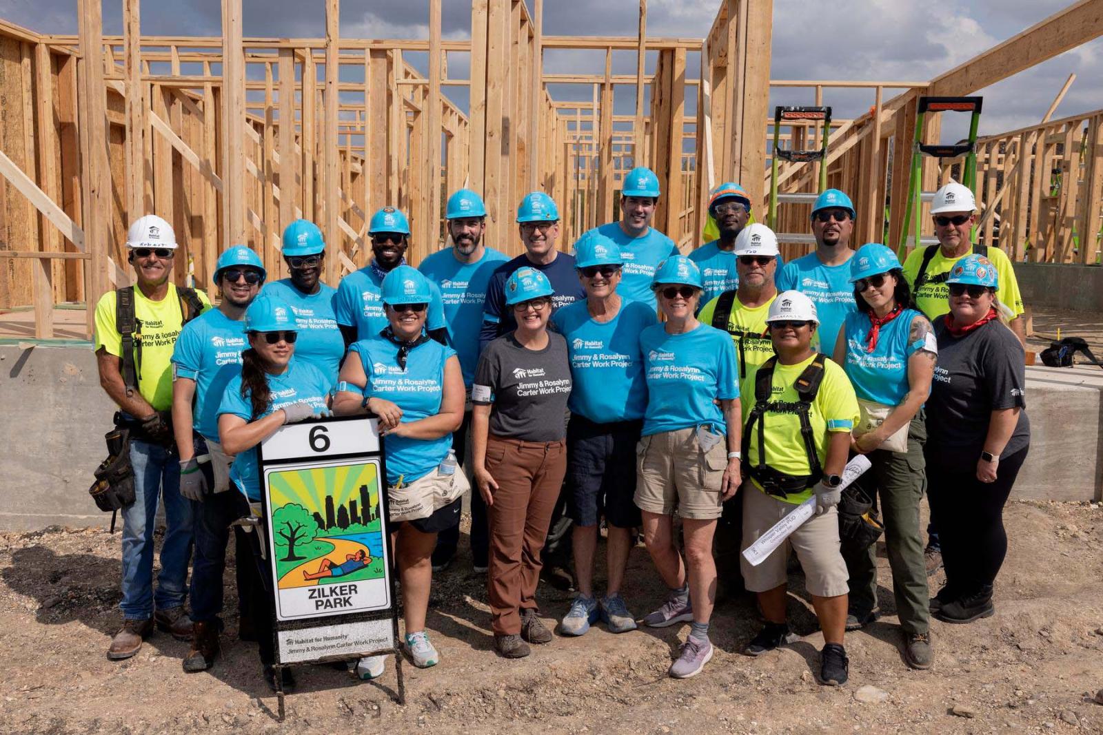 House six volunteers stand in a large group in front of the frame of a house at Carter Work Project in Austin, Texas.