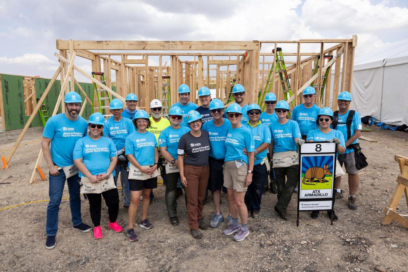 House eight volunteers stand in a large group in front of the frame of a house at Carter Work Project in Austin, Texas.