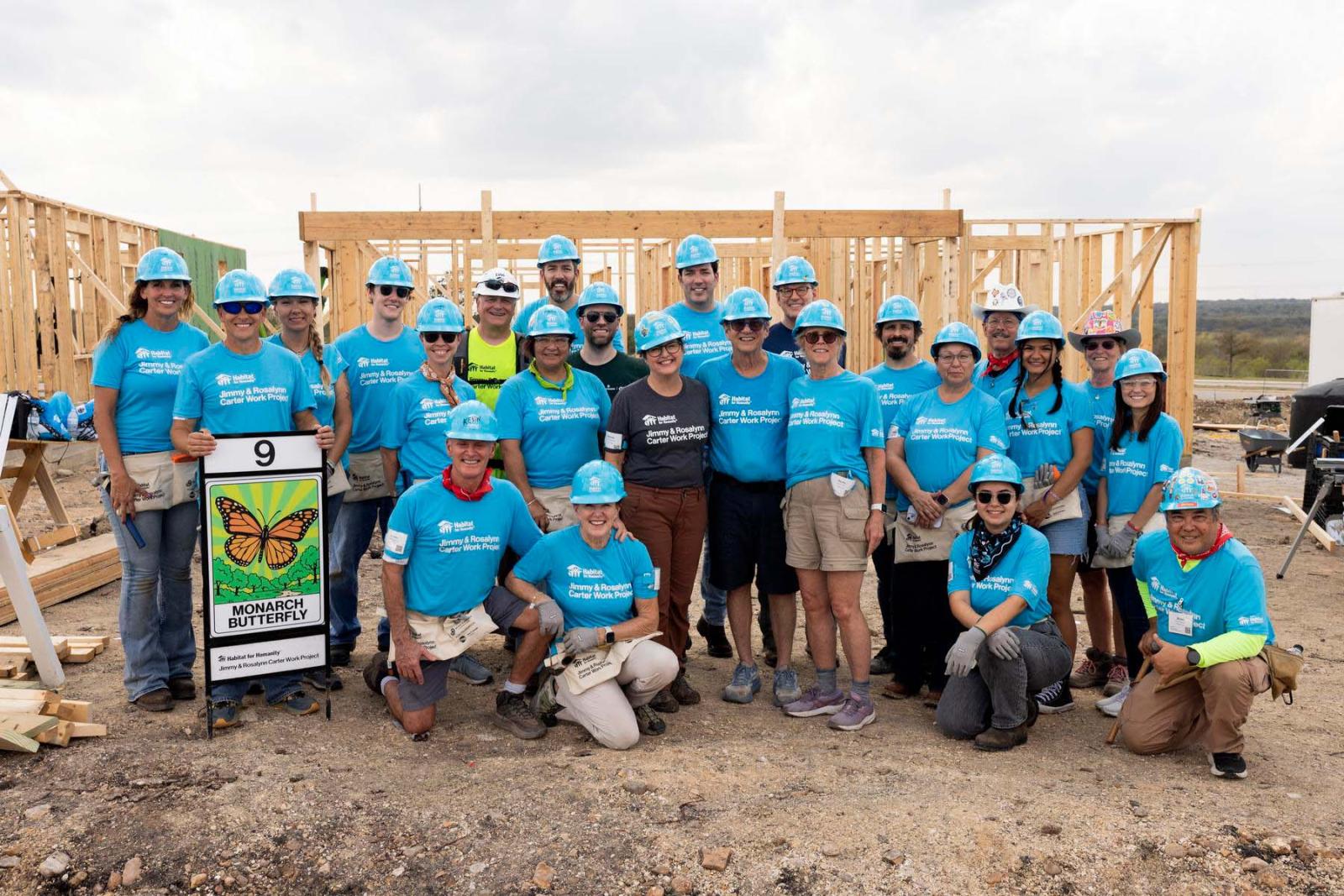 House nine volunteers stand in a large group in front of the frame of a house at Carter Work Project in Austin, Texas.