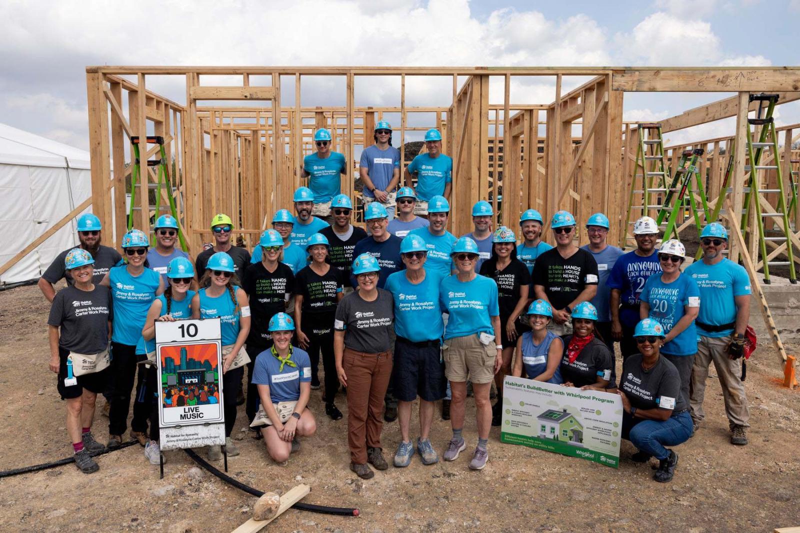House ten volunteers stand in a large group in front of the frame of a house at Carter Work Project in Austin, Texas.