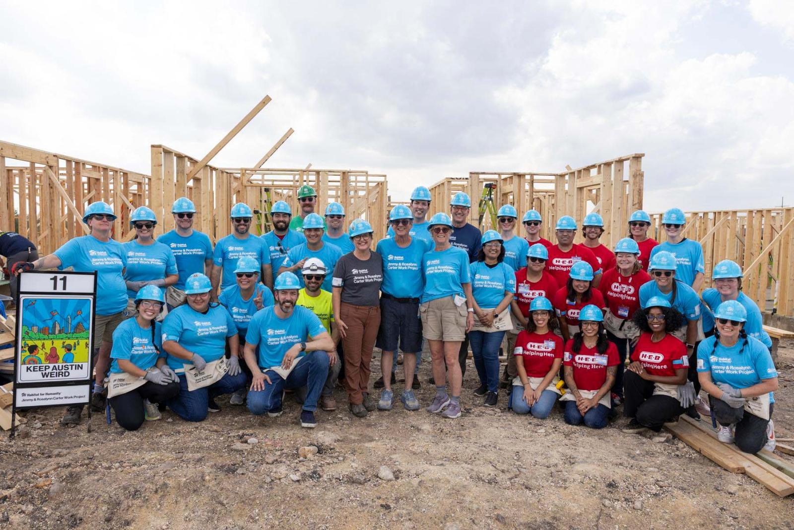 House eleven volunteers stand in a large group in front of the frame of a house at Carter Work Project in Austin, Texas.