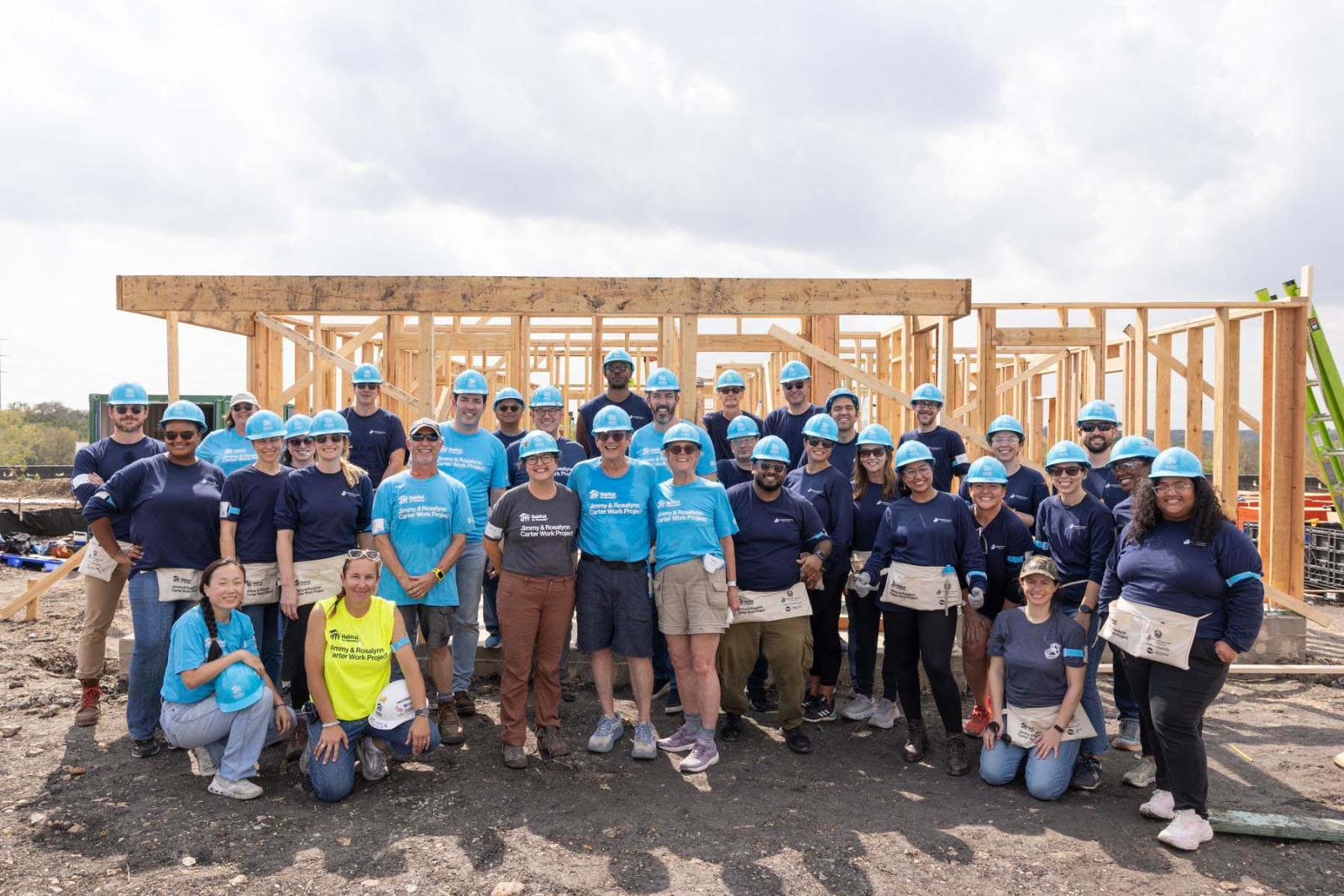 House fifteen volunteers stand in a large group in front of the frame of a house at Carter Work Project in Austin, Texas.
