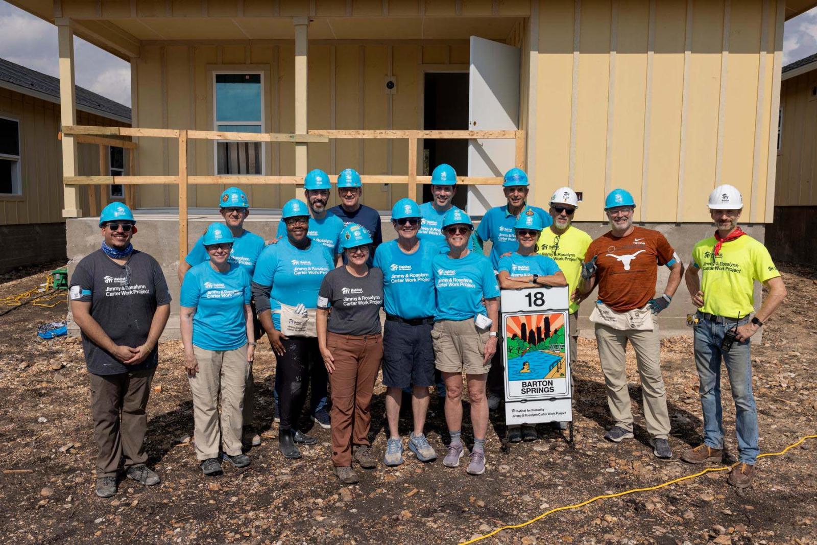 House eighteen volunteers stand in a large group in front of the frame of a house at Carter Work Project in Austin, Texas.