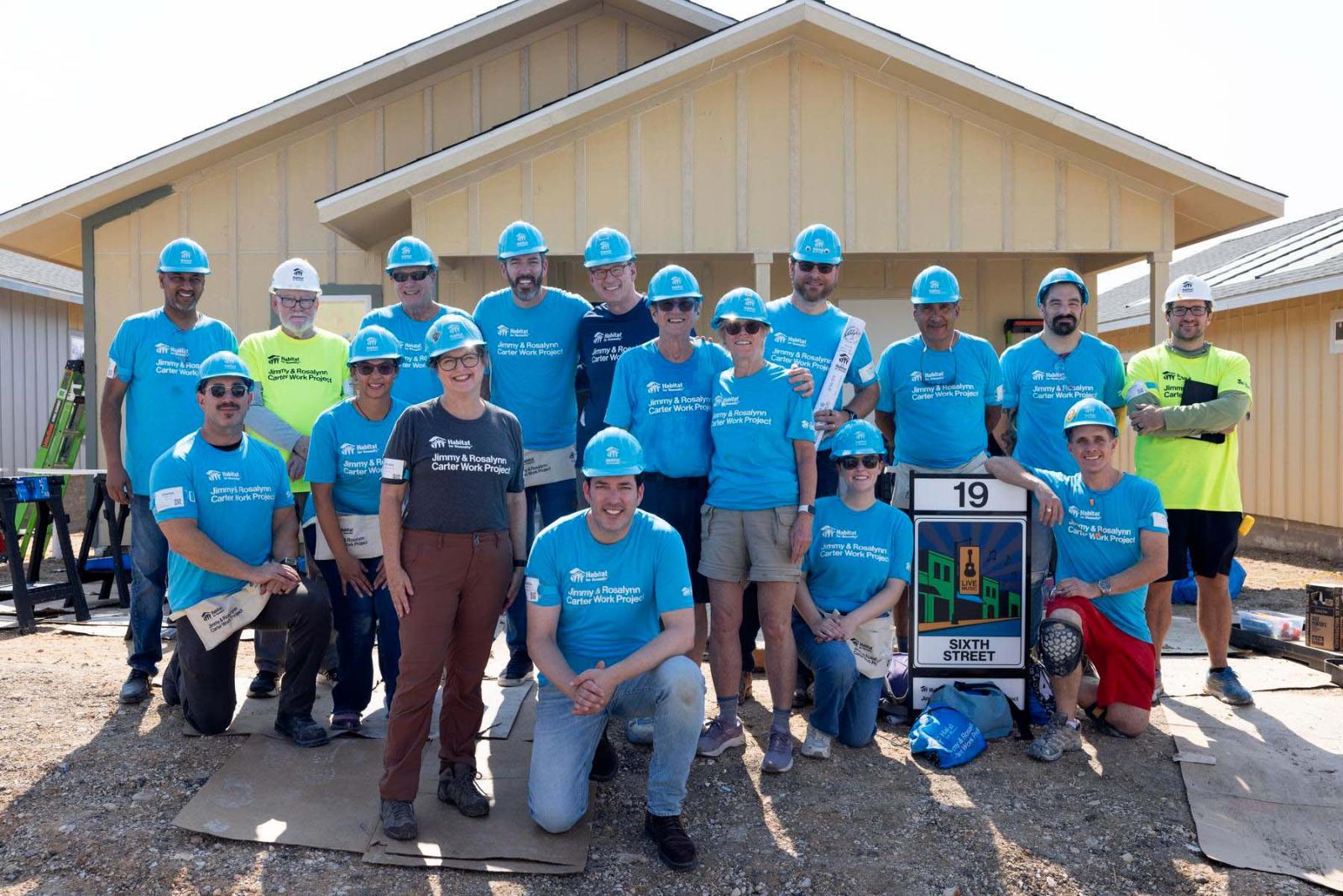 House nineteen volunteers stand in a large group in front a house at Carter Work Project in Austin, Texas.