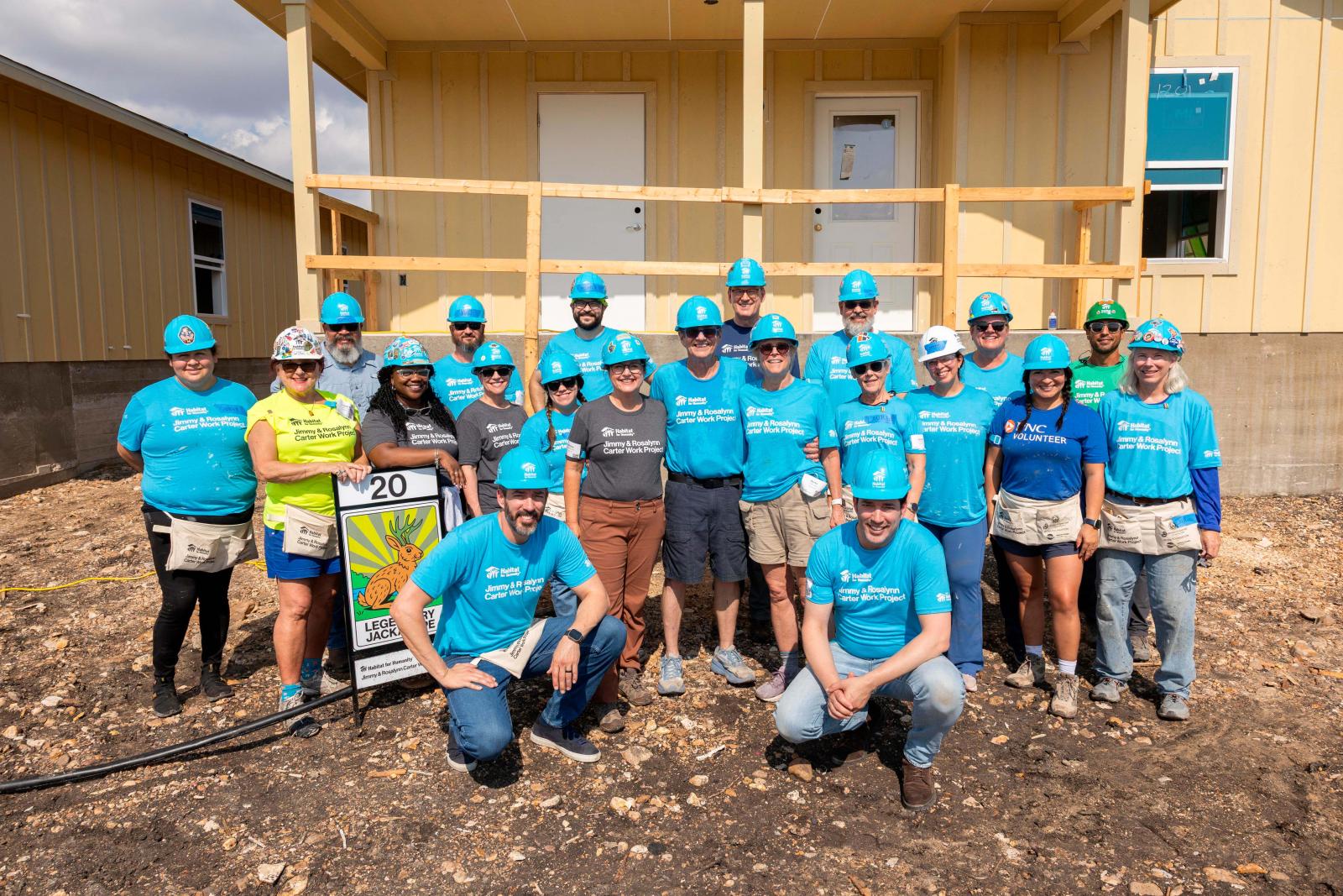House twenty volunteers stand in a large group in front a house at Carter Work Project in Austin, Texas.