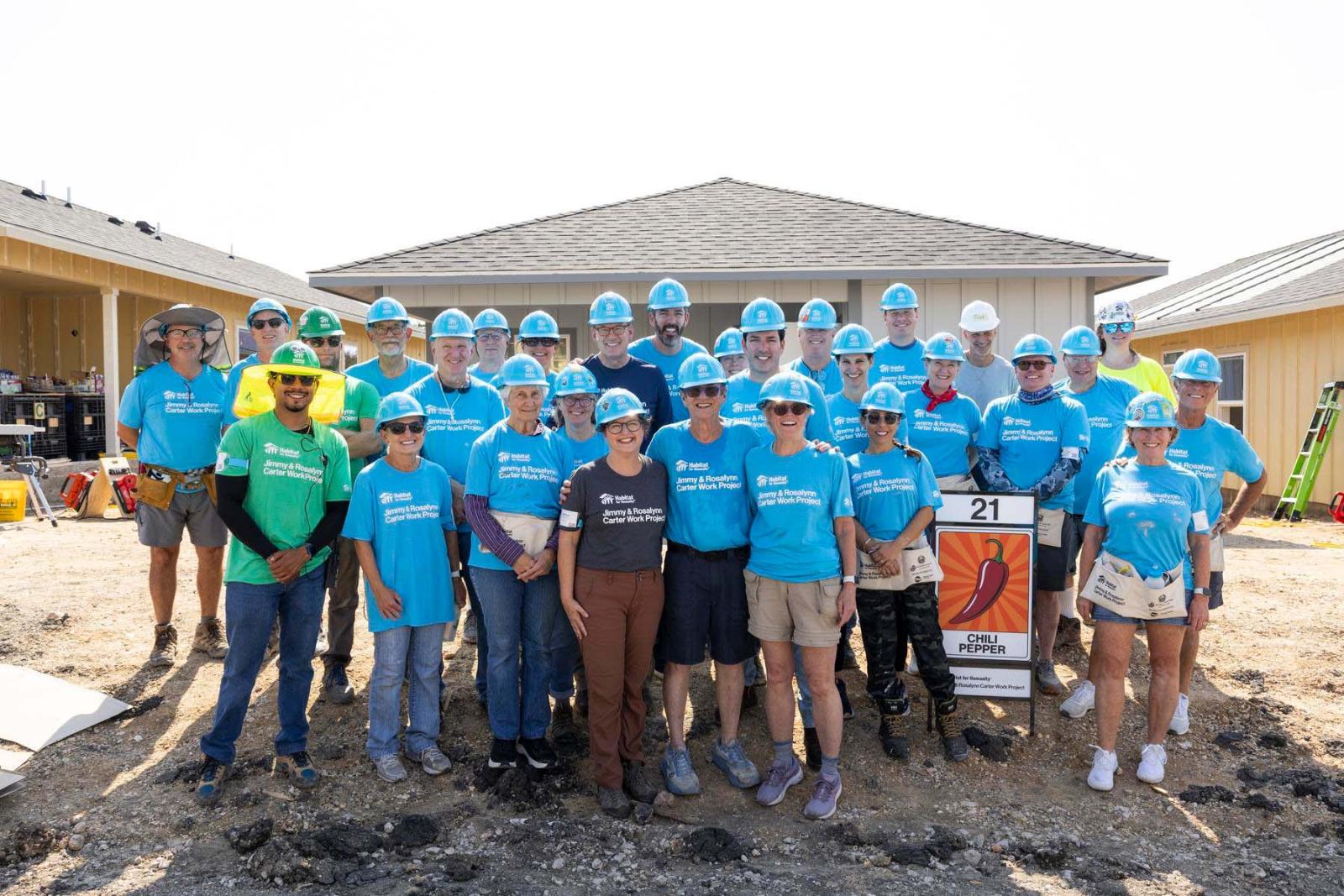 House twenty-one volunteers stand in a large group in front a house at Carter Work Project in Austin, Texas.