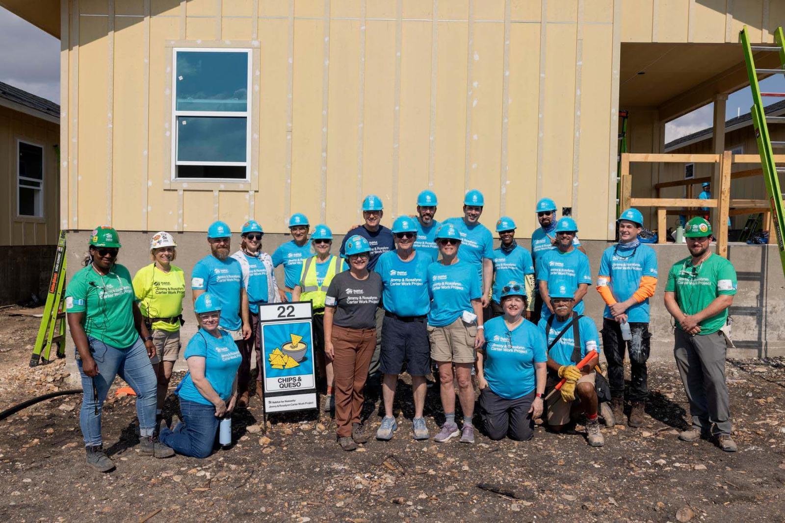 House twenty-two volunteers stand in a large group in front a house at Carter Work Project in Austin, Texas.