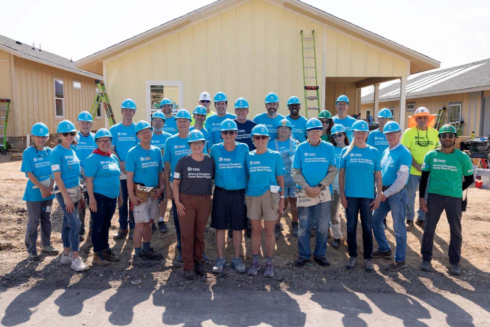 House twenty-three volunteers stand in a large group in front a house at Carter Work Project in Austin, Texas.