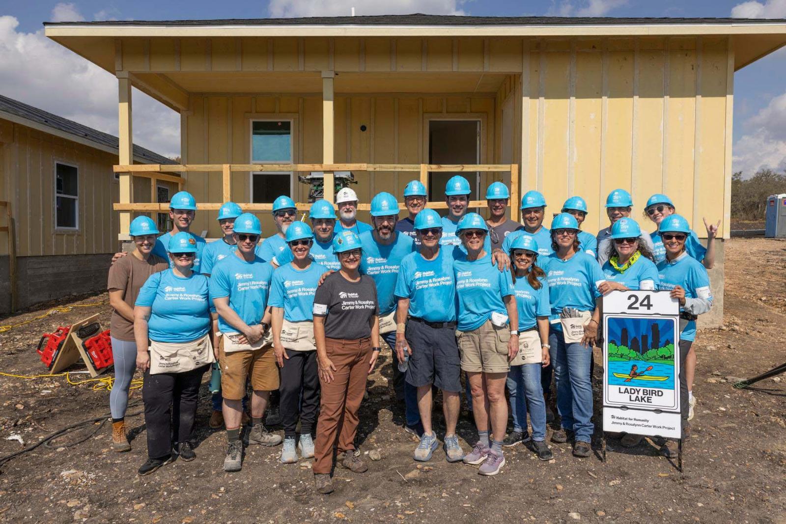 House twenty-four volunteers stand in a large group in front a house at Carter Work Project in Austin, Texas.