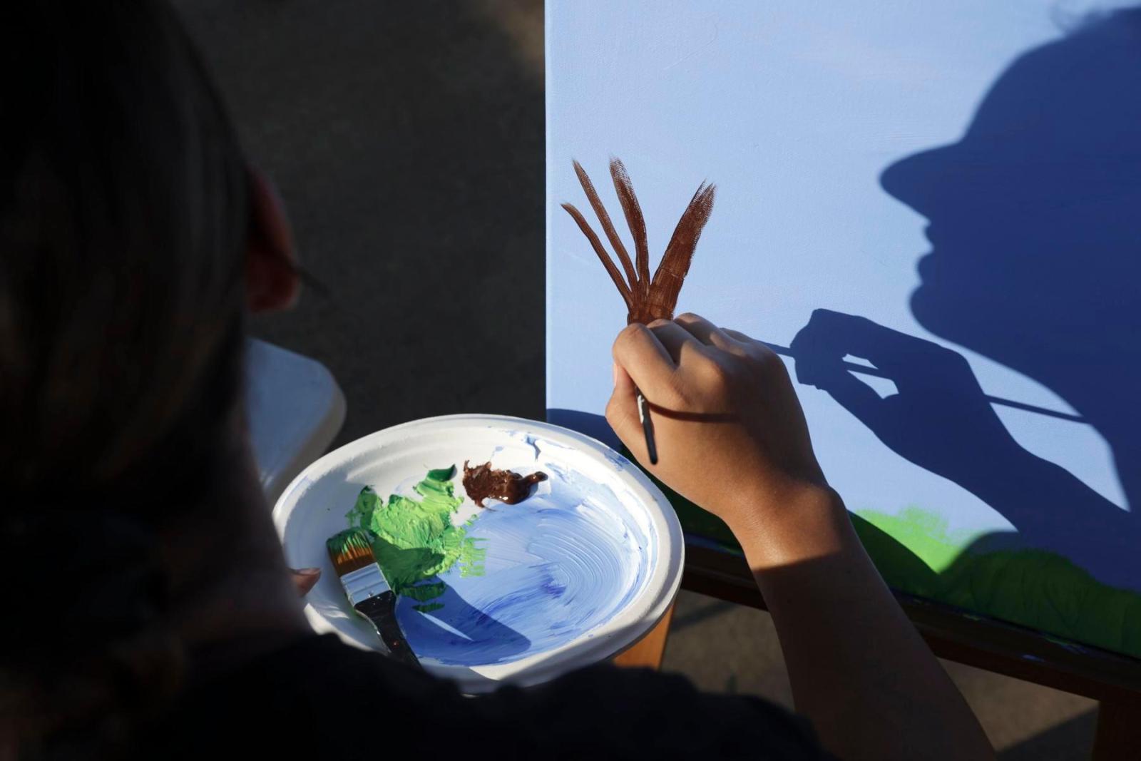 The shadow of a volunteer is seen on a wall as they paint the side of a house.