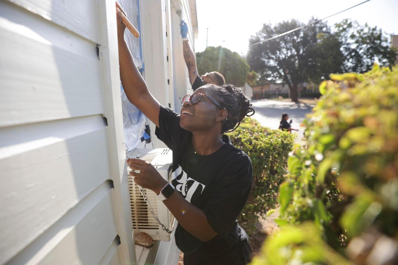 A volunteer reaches up to pain house siding.