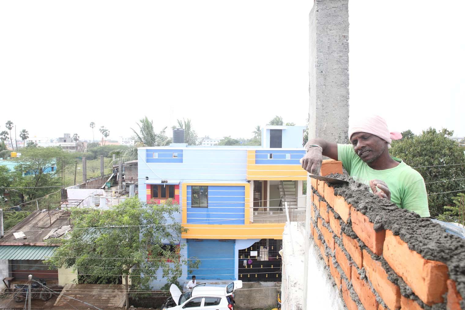A worker in a green shirt paves bricks at the top of a building. 
