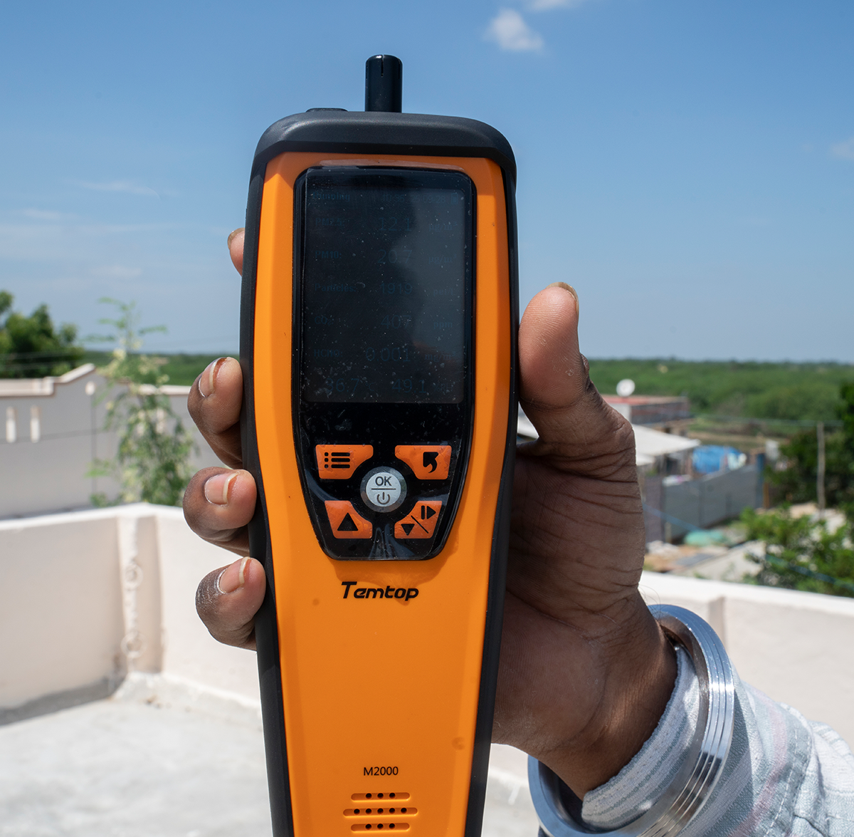 An engineer holds up an orange tool to check the temperature of a roof that is painted white.