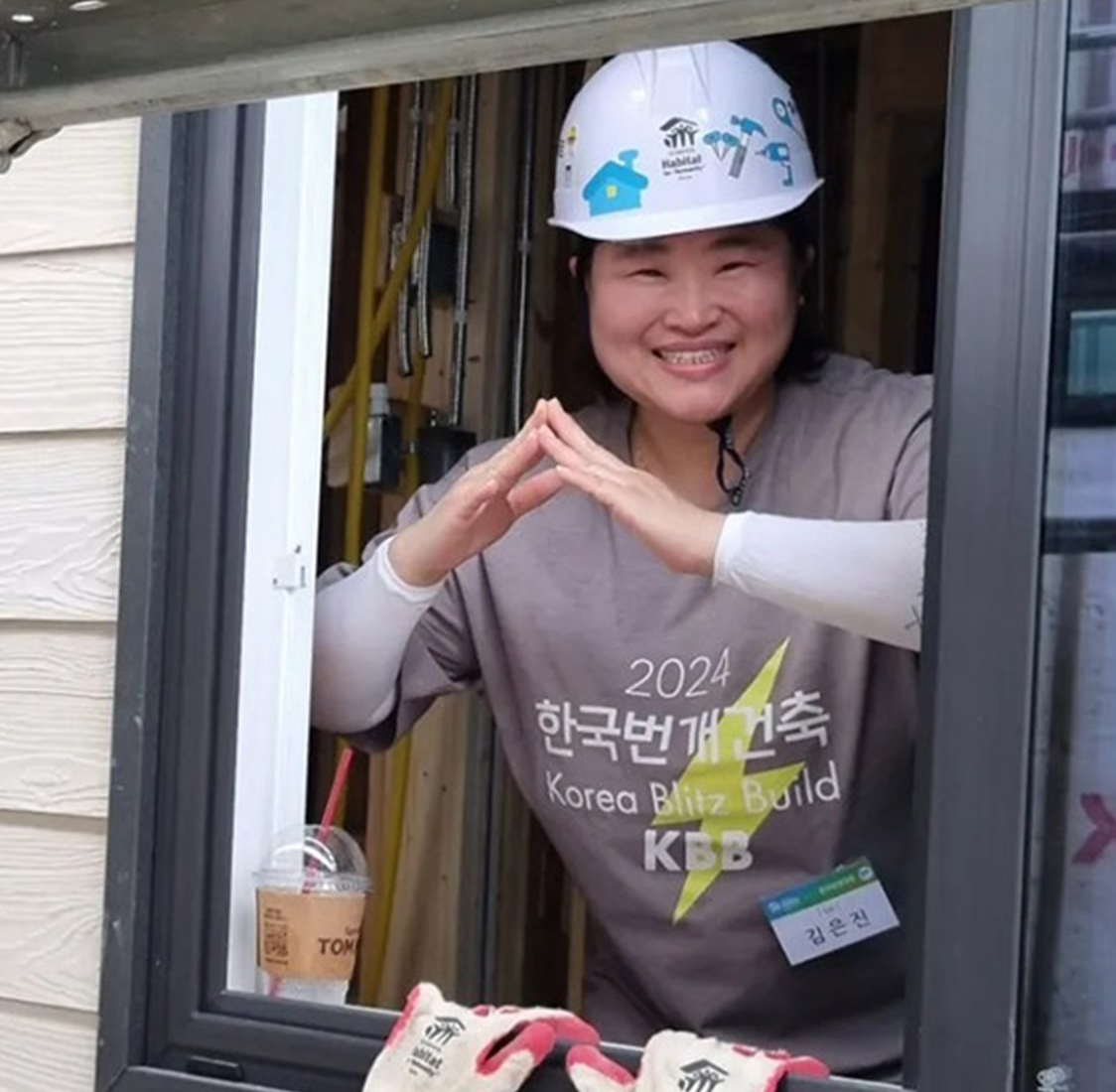 A woman stands, smiling, in a white helmet in the window of a newly built home.