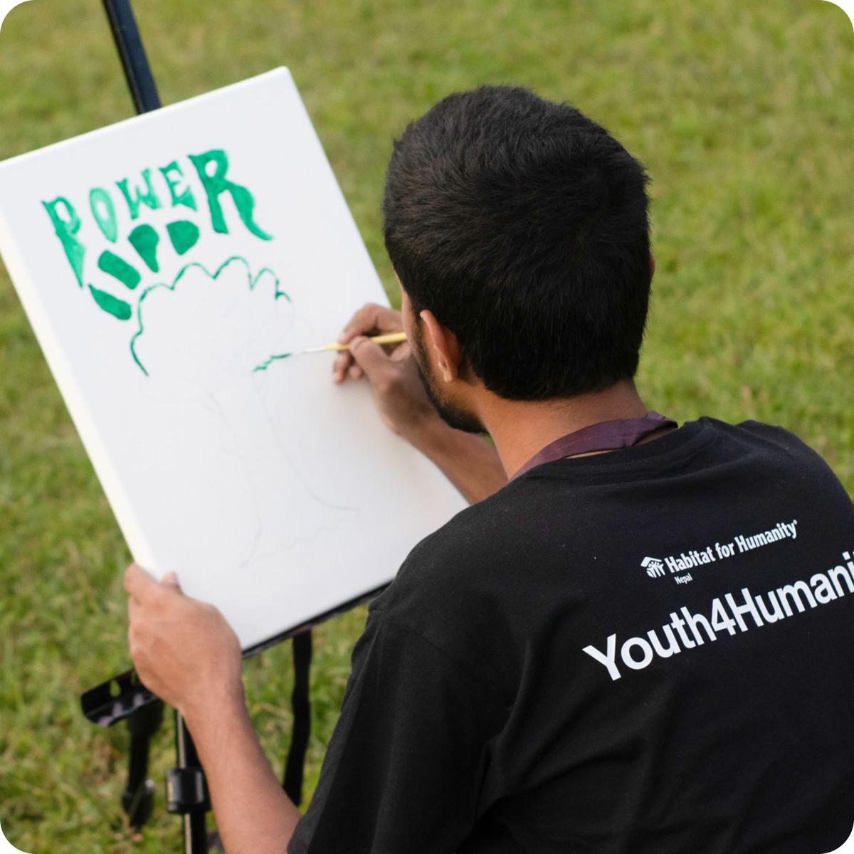 Man in black t-shirt painting on a canvas in a grassy field.