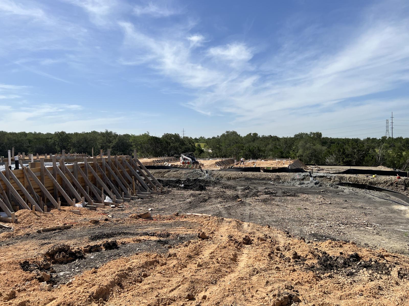 A construction site with concrete foundation forms rising out of an expanse of dirt.