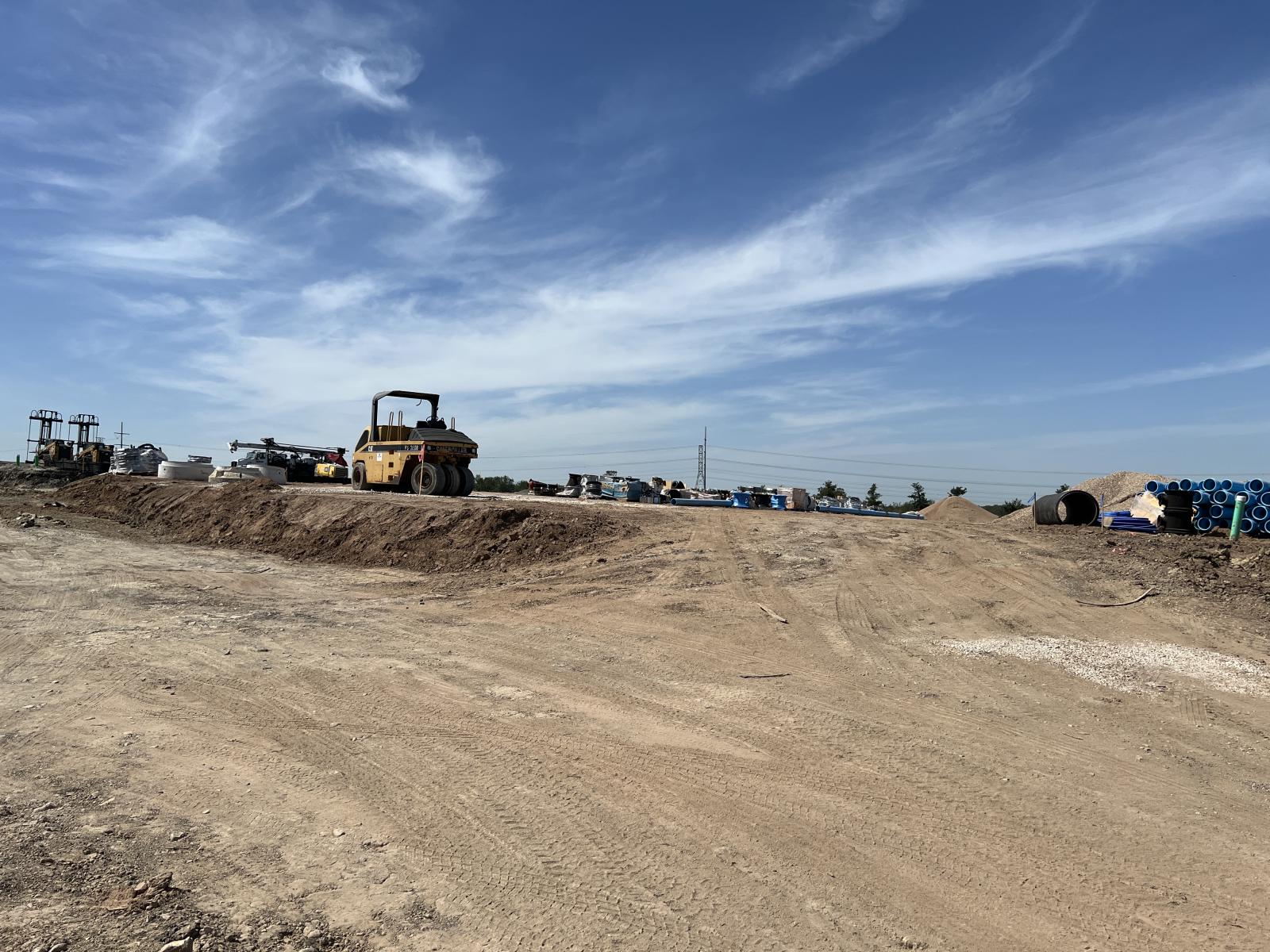 An expanse of cleared land with heavy machinery on the horizon, with a blue sky behind.