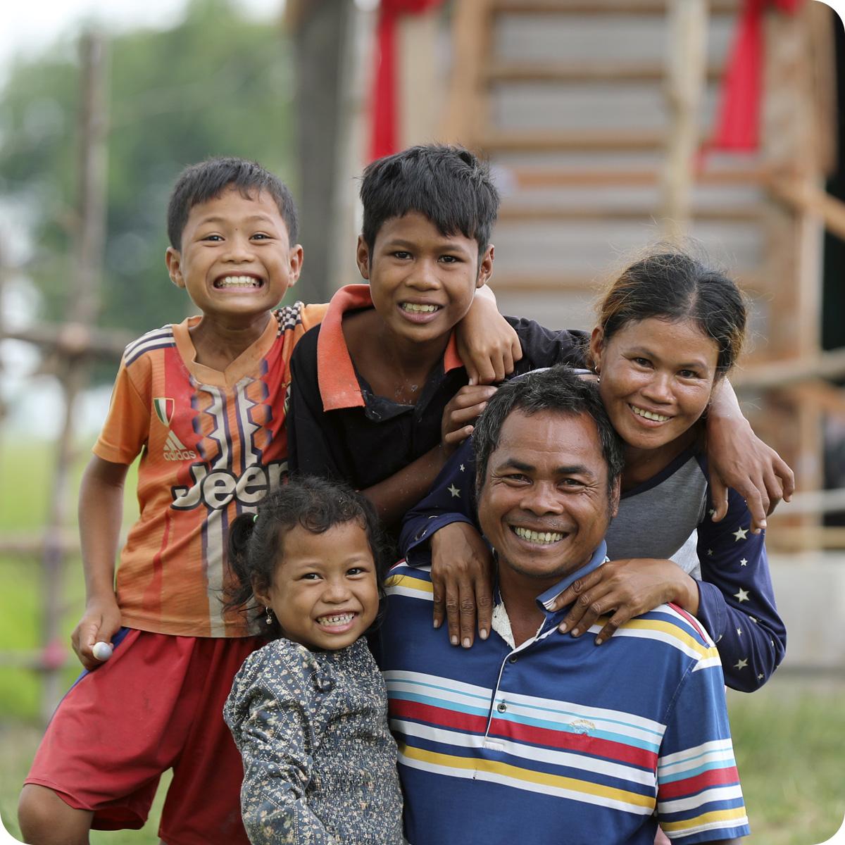 Family of five smiles at the camera in front of their home.