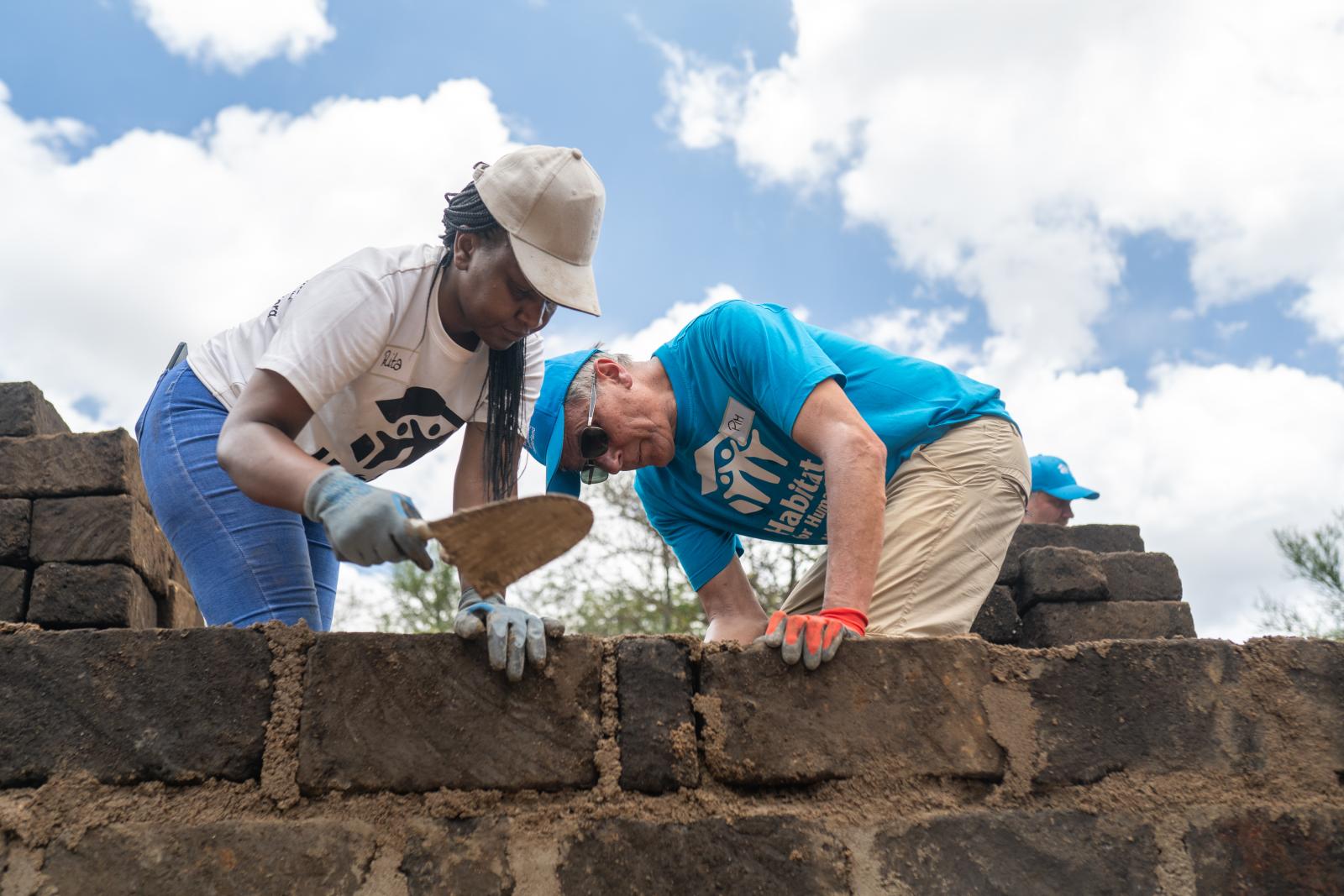Two volunteers (woman, left) (man, right) in Habitat shirts and hats building a stone fence.