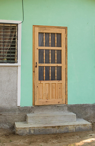 Una puerta principal de madera de color marrón claro rodeada de paredes pintadas de color verde brillante.