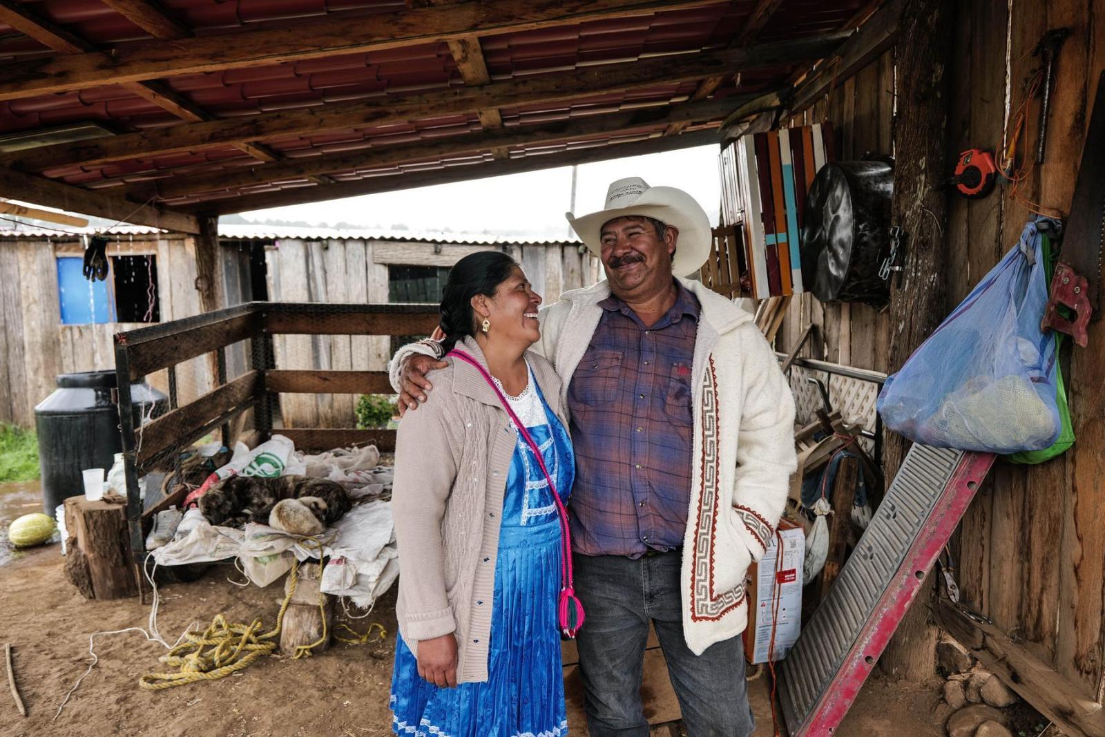 A man and a woman stand in a barn holding on to one another and smiling.